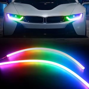 May include: A white sports car with illuminated headlights displaying a rainbow gradient. Below, two curved LED light strips glow with a spectrum of colors, including red, green, and blue, against a dark background. Automotive lighting.