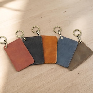 Peut inclure: Cinq porte-cartes rectangulaires en cuir aux coins arrondis, chacun doté d'un anneau brisé et d'un mousqueton en métal couleur bronze fixés sur le dessus. Les porte-cartes sont de couleur brun rougeâtre, noir, orange, bleu et brun clair.