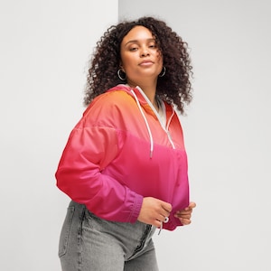 May include: A cropped windbreaker jacket featuring a vibrant gradient color scheme that transitions from orange at the top to pink and deep magenta at the bottom. The jacket includes a quarter-zip front, a hood with white drawstrings, and long sleeves.
