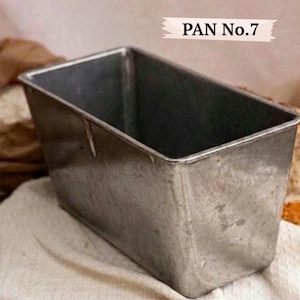 May include: A rectangular metal loaf pan with a weathered silver finish. The pan features a deep, open-top design with straight sides and a rolled rim. A label attached to the upper right corner of the image displays the text PAN No.7 in black.