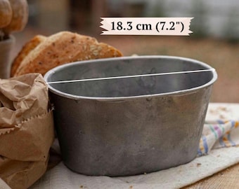 May include: An oval-shaped metal baking pan with a weathered, matte gray finish. A white line indicates a diameter of 7.2 inches, with the text 18.3 cm (7.2") displayed above the pan, showing the measurement of the opening.