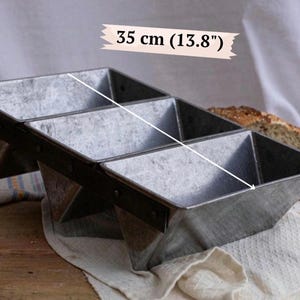 May include: A metallic triple loaf baking pan with a weathered finish, featuring three connected rectangular compartments. A white graphic line indicates a length of 35 cm across the top of the pan, with the text 35 cm (13.8") visible above the unit.