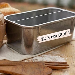 May include: A rectangular silver-colored metal loaf pan with a smooth interior and a rolled rim. The pan features a clear measurement indicator printed on the side, showing a length of 8.8 inches, which corresponds to a metric length of 22.5 cm.