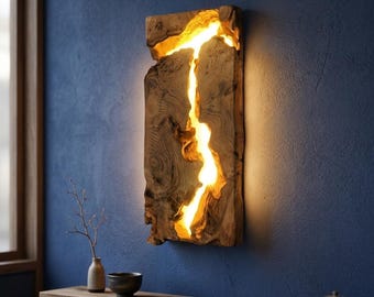 May include: A rectangular wooden wall light fixture with a natural, rough-hewn appearance. The light emanates from a central, irregular channel, creating a warm, inviting glow. The fixture is mounted on a blue wall, adding a rustic touch to the space.
