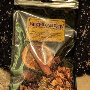 May include: A clear plastic pouch containing a simmer pot blend labeled Stir The Cauldron. The ingredients include whole orange slices, cinnamon sticks, hibiscus flowers, dried cranberries, juniper berries, black cardamom pods, mugwort, and vanilla bean.
