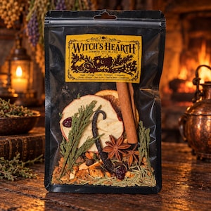 May include: A black resealable pouch containing a Witch's Hearth simmer pot blend. The yellow label features the text "Witch's Hearth" and a list of ingredients including apple, orange, cedar, rosemary, cinnamon, cloves, allspice, star anise, vanilla bean, and cranberries, which are visible inside the clear plastic window.