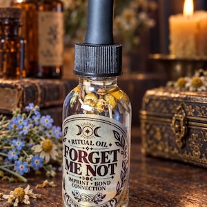 May include: A clear glass dropper bottle containing liquid and dried chamomile flowers. The label features the text "RITUAL OIL FORGET ME NOT IMPRINT BOND CONNECTION CURIO NOCTURNE" with moon and floral illustrations. It has a black rubber dropper top.
