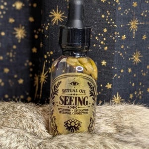 May include: A clear glass dropper bottle filled with liquid and dried botanicals. The gold label features an eye icon and the text: RITUAL OIL SEEING INTUITION DIVINATION SPIRITUAL CONNECTION. The bottle has a black dropper cap.
