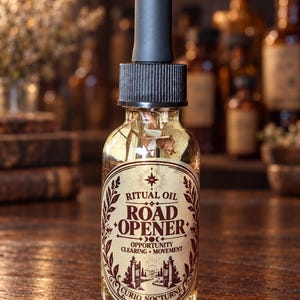 May include: A clear glass dropper bottle filled with light-colored oil and botanical pieces. The label features the text RITUAL OIL ROAD OPENER OPPORTUNITY CLEARING MOVEMENT CURIO NOCTURNE and an illustration of an open gate on a path.