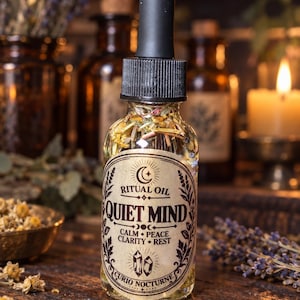 May include: A clear glass dropper bottle filled with oil and dried botanicals. The label features the text RITUAL OIL QUIET MIND CALM PEACE CLARITY REST CURIO NOCTURNE with moon, star, and crystal illustrations. It has a black dropper cap.