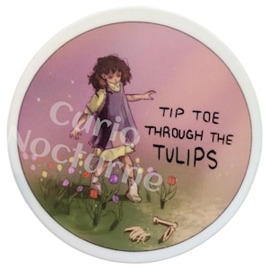May include: A round, white button with a whimsical illustration. It features a girl in a purple dress and yellow shirt, walking through a field of tulips. The text "Tip Toe Through The Tulips" is displayed. The button has the text "Curio Nocturne" on the left side.