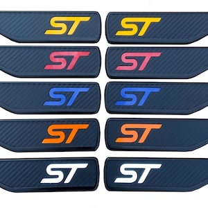 May include: Ten black car door sill protectors with a carbon fibre texture. Each features the letters "ST" in yellow, pink, blue, orange, and white. The protectors are angled and designed to fit a car door.