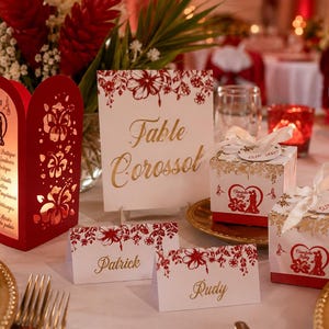 Op de afbeelding: Een tafelsetting voor een bruiloft met rode en gouden accenten. Inclusief een rode menukaart, tafelkaart, naambordjes en geschenkdozen. Bloemschikkingen en kaarsen dragen bij aan de feestelijke sfeer.