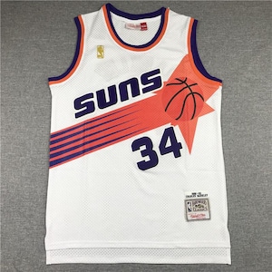 Può includere: Canotta da basket bianca con la scritta "SUNS" in viola e il numero "34" in viola. La canotta presenta dettagli arancioni e viola e una grafica di pallone da basket. Una piccola etichetta è visibile in basso.
