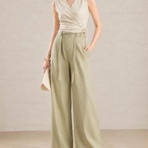 Puede incluir: Un top sin mangas cruzado con un sutil estampado floral, combinado con pantalones de cintura alta y pernera ancha en un suave tono verde. El conjunto incluye un cintur&oacute;n a juego y un clutch de color neutro, creando un conjunto coordinado y elegante.
