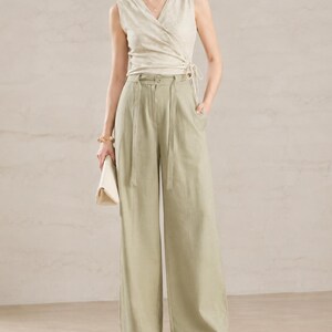 Puede incluir: Una mujer con un top cruzado beige y pantalones de pierna ancha verde claro. El top tiene cuello en V y cierre de lazo. Los pantalones tienen cintura alta y cintur&oacute;n a juego. Tambi&eacute;n lleva un clutch blanco y sandalias blancas.