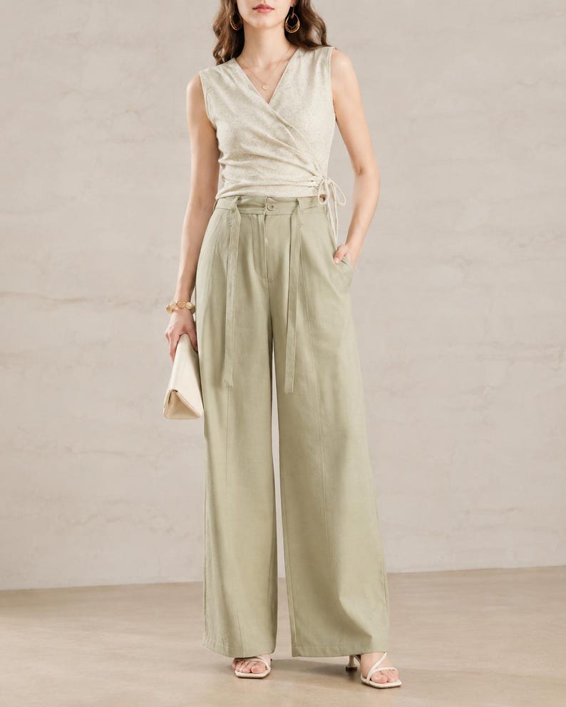 Puede incluir: Una mujer con un top cruzado beige y pantalones de pierna ancha verde claro. El top tiene cuello en V y cierre de lazo. Los pantalones tienen cintura alta y cintur&oacute;n a juego. Tambi&eacute;n lleva un clutch blanco y sandalias blancas.
