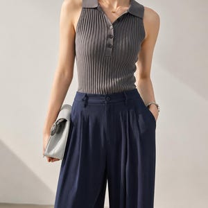 Puede incluir: Un top sin mangas de punto acanalado gris con cuello polo y cierre de botones, combinado con pantalones de pierna ancha azul marino. El conjunto es una versi&oacute;n moderna de prendas separadas cl&aacute;sicas.