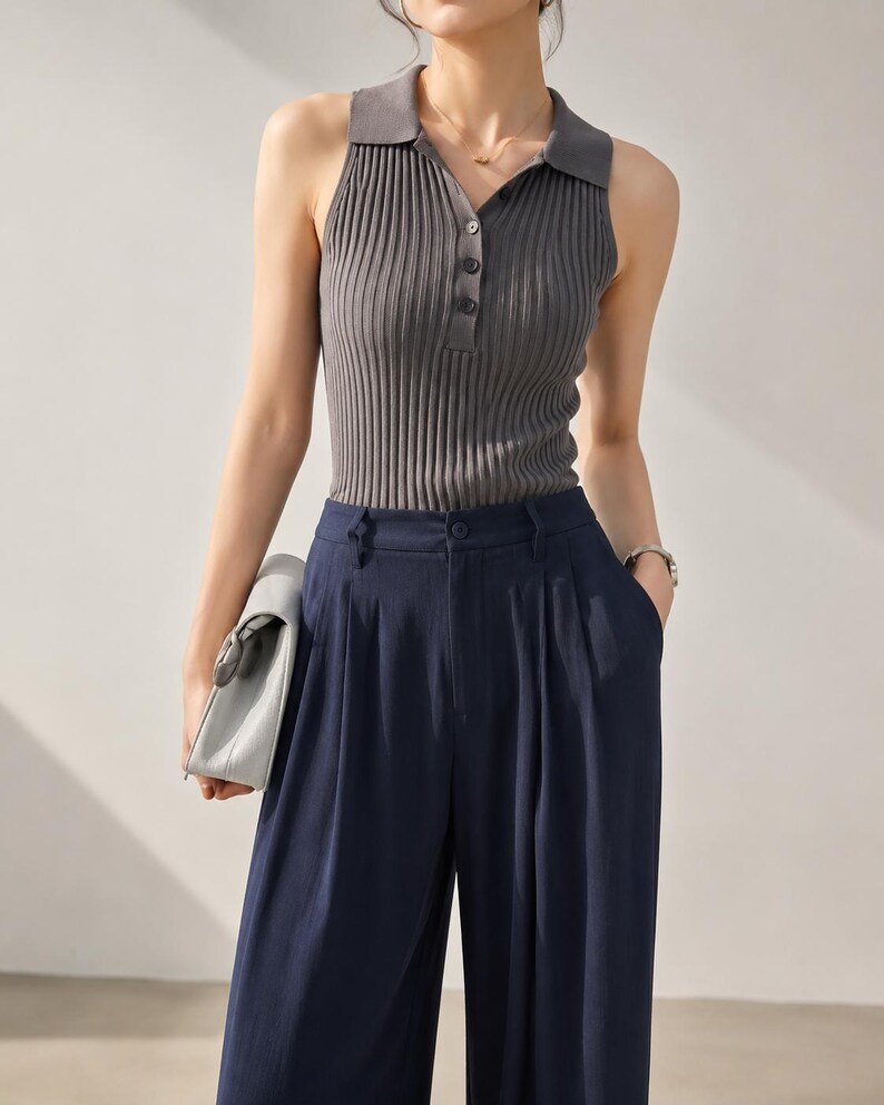 Puede incluir: Un top sin mangas de punto acanalado gris con cuello polo y cierre de botones, combinado con pantalones de pierna ancha azul marino. El conjunto es una versi&oacute;n moderna de prendas separadas cl&aacute;sicas.