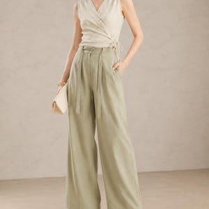 Puede incluir: Un top sin mangas cruzado y pantalones de pernera ancha en una paleta de colores suaves y neutros. El top tiene cuello en V y cierre de lazo. Los pantalones de cintura alta son de un verde apagado con pliegues y cintur&oacute;n a juego. El conjunto se completa con tacones blancos y un clutch crema.