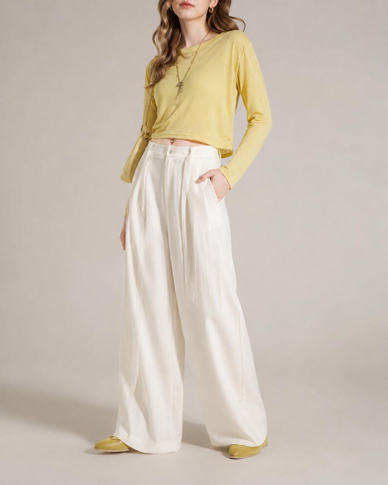 Puede incluir: Un conjunto femenino con una blusa amarilla p&aacute;lida de manga larga y pantalones blancos de pernera ancha. La blusa tiene cuello redondo y los pantalones est&aacute;n plisados. El conjunto se completa con bailarinas amarillas y un collar largo.