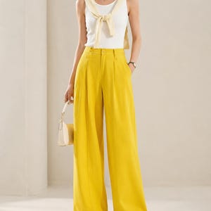 Puede incluir: Conjunto femenino que presenta una camiseta sin mangas blanca con un su&eacute;ter amarillo atado al cuello, combinado con pantalones amarillos de cintura alta y pernera ancha. El conjunto se completa con zapatillas blancas y un peque&ntilde;o bolso de mano color crema.