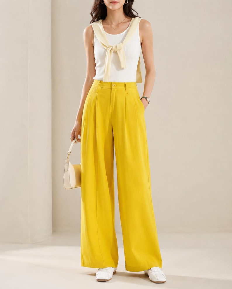 Puede incluir: Conjunto femenino que presenta una camiseta sin mangas blanca con un su&eacute;ter amarillo atado al cuello, combinado con pantalones amarillos de cintura alta y pernera ancha. El conjunto se completa con zapatillas blancas y un peque&ntilde;o bolso de mano color crema.