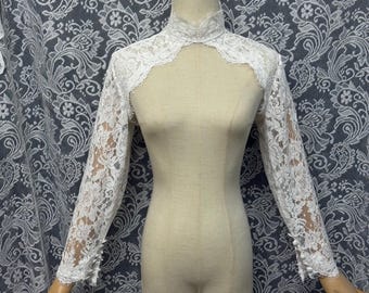 Bolero nupcial de encaje con cuello alto desmontable y mangas largas, elegante sobre el vestido de novia.
