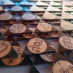 Puede incluir: Colección de baldosas triangulares de madera con bordes marrón oscuro y negro. Cada baldosa presenta un círculo de madera clara con un símbolo negro e intrincado. Las baldosas están dispuestas en un patrón en capas.