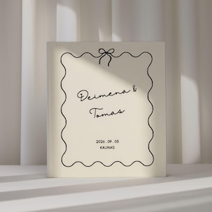 May include: A cream-colored rectangular book with a black line-drawn scalloped border and a bow at the top. The text reads Deimena & Tomas, followed by the date 2026.09.05 and the location KAUNAS in black lettering centered on the front cover.