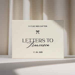 Puede incluir: Una caja rectangular de color crema con texto en negro que dice FUTURE MRS GAYTON, un pequeño icono de lazo, LETTERS TO Francesca y la fecha 17. 09. 2026. La caja tiene una textura suave similar a la tela y un diseño limpio.