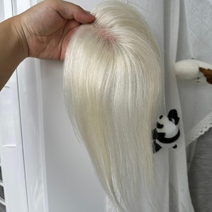 Könnte beinhalten: Ein Haarteil mit glattem, platinblondem Haar und einer sichtbaren Monofilament-Basis am Oberkopf. Das Haar ist glatt und geschmeidig und weist durchgehend einen hellen, eisblonden Farbton auf, der sich vom Bereich des Scheitels nach unten erstreckt.
