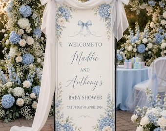 May include: A vertical welcome sign for a baby shower featuring blue and white hydrangea floral illustrations, a light blue ribbon graphic, and text reading: WELCOME TO Maddie AND Anthony's BABY SHOWER SATURDAY 08 APRIL 2026, draped with white fabric.
