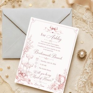 Könnte beinhalten: Eine rechteckige weiße Einladungskarte mit rosa Text und Illustrationen. Sie zeigt eine Schleife, einen Stapel Champagnergläser und eine offene Ringschatulle mit einem Ring. Der Text lautet For Ashley, Bridesmaids Brunch, Saturday, July 18, 2026, 11:30 AM, The Garden Room, Will you be my Maid of Honor?, und Love, Emma.