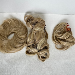 May include: Three blonde hair extensions and accessories. One is a circular hair bun piece, one is a long wavy hair extension with a dark brown claw clip, and one is a smaller wavy hair piece attached to a tortoiseshell-colored claw clip.