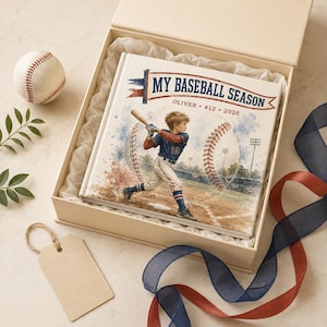Könnte beinhalten: Ein quadratisches Hardcover-Buch mit dem Titel MY BASEBALL SEASON und einer Aquarellillustration eines Kindes beim Schlag auf einem Spielfeld, personalisiert mit OLIVER #12 2026. Das Buch liegt in einer beigen Geschenkbox mit einem Baseball.