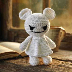 May include: A handmade white crochet doll with a mouse-like head and small, round ears. The doll has black eyes and a stitched smile. It is wearing a simple dress and stands on a wooden surface.