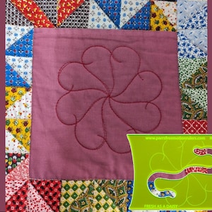 Op de afbeelding: Een patchwork quilt vierkant met een centraal bloemenontwerp gestikt in rode draad. Het vierkant is omgeven door kleurrijke stoffen driehoeken en patronen. Een groene quilt sjabloon staat in de rechter benedenhoek, met de tekst "FRESH AS A DAISY".