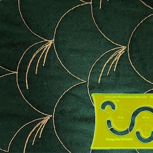 May include: Dark green fabric with a gold, curved, quilted pattern. A yellow quilting template with curved cutouts and text is in the lower right corner. The template has the text "www.pamsfree motionrulers.com" and "Design No. 8043890".