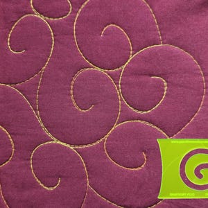 May include: A deep plum-colored fabric featuring continuous gold-colored machine-stitched swirl patterns. A lime green plastic quilting template with a spiral cutout and the text "RHAPSODY PLUS" is positioned in the bottom right corner.