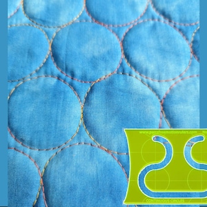 May include: Close-up of a quilted fabric with large, light blue circles stitched with orange and yellow thread. A green and yellow quilting template with the text "CONTINUOUS CIRCLES" is in the lower right corner.