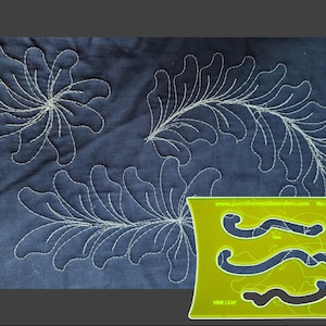 May include: A lime green plastic quilting template with three wavy cutouts and the text "www.parsfreemotionrulers.com No.3b VINE LEAF" printed on it, positioned over dark blue fabric featuring white stitched floral and vine patterns.