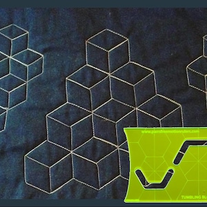 May include: Dark blue fabric with a repeating pattern of white stitched cubes. A green acrylic quilting template with the text "TUMBLING BLOCKS" and website address is in the lower right corner. The template has two curved cutouts.