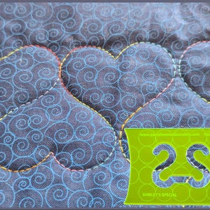 May include: Close-up of a quilted fabric with a heart-shaped pattern in blue and white. The stitching is in yellow, red, and white thread. A green stencil with the number 2S and the text "SHIRLEY'S SPECIAL" is in the lower right corner.