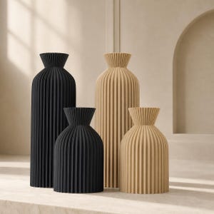 May include: Four decorative vases in varying sizes and colors. Two are black, and two are beige. Each vase has a ribbed, vertical design and a flared, ruffled top. The vases are arranged on a neutral surface.
