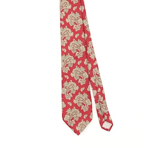 Può includere: Una cravatta con uno sfondo rosso vivace decorato con un motivo paisley ripetitivo color crema e marrone chiaro. Il tessuto presenta una stampa coerente di motivi a forma di goccia lungo tutta la lunghezza dell'accessorio.