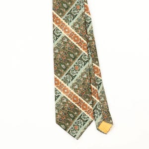 Könnte beinhalten: Eine Krawatte mit einem sich wiederholenden diagonalen Muster in Olivgrün, Salbei und gebranntem Orange. Das Design besteht aus abwechselnden breiten Bändern mit komplexen Blumen- und Geometriemotiven, getrennt durch schmale orangefarbene Paisleystreifen.