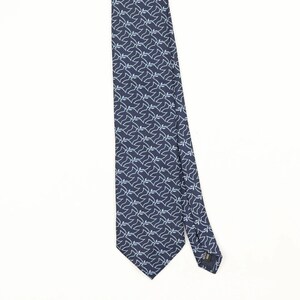 May include: A dark navy blue necktie featuring a repeating geometric pattern of light blue, thin, interconnected line shapes. The tie has a pointed end and a visible black fabric label attached to the back side of the narrow tail section.