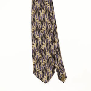 Peut inclure: Une cravate présentant un motif répétitif de lignes verticales ondulées dans des tons de violet, noir et or. Le tissu a une texture lisse avec un léger éclat, et une petite étiquette rectangulaire est visible au dos de l'extrémité étroite.