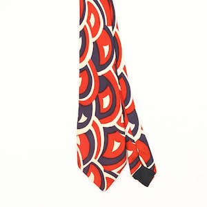 Può includere: Una cravatta con un motivo geometrico ripetitivo di semicerchi sovrapposti in rosso vivace, blu navy scuro e bianco sporco. Il tessuto presenta una consistenza liscia con una punta sul fondo e una fodera scura visibile sul bordo.
